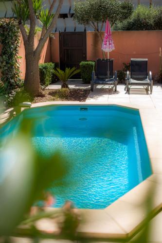 - une piscine bleue avec 2 chaises et un parasol dans l'établissement Chambre Taza, Riad 1 Couple only au village naturiste, au Cap d'Agde