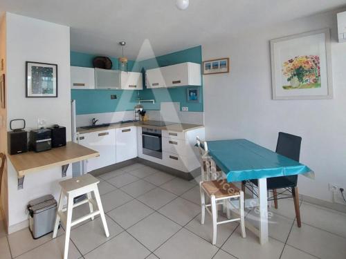 une petite cuisine avec une table bleue et des chaises dans l'établissement T2 avec terrasse, clim dans le salon, parking a quelques pas des plages, à Sète