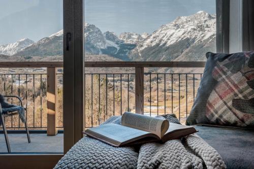 a book on a bed with a view of mountains at Arnica Alpin Lodge in Cavedago