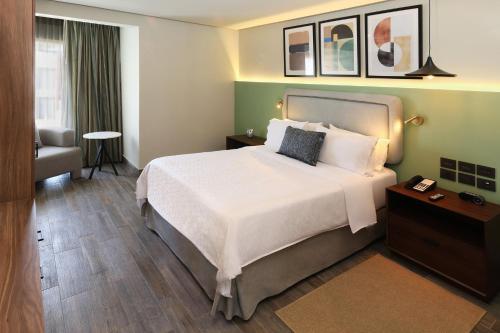 a hotel room with a large bed and a chair at voco Hermosillo by IHG in Hermosillo