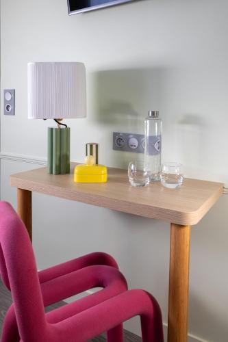 a wooden table with a lamp and a pink chair at Hotel La Folie des Pres - Saint-Germain-des-Pres in Paris