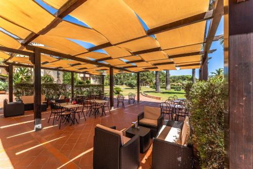 a patio with tables and chairs under a wooden umbrella at Classical Res Baia Delle Palme Prem Bilo 4 person in Santa Margherita di Pula