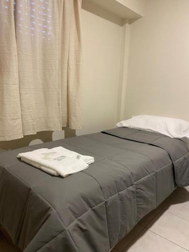 a bed with a gray blanket and a window at Hotel Olavarria in Olavarría
