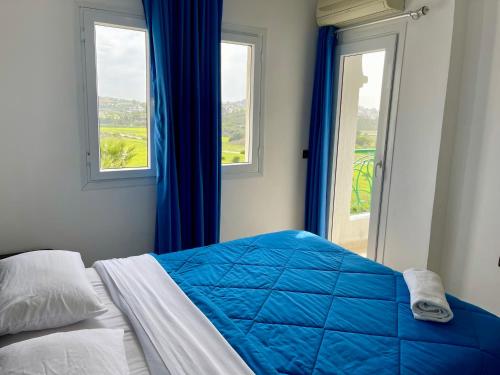 a bedroom with a bed with a blue comforter and two windows at Appartement de vacances piscines et plage in Tangier