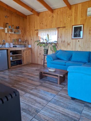 Una sala de estar con un sofá azul y una mesa. en Cabaña Refugio Magenta con tinaja caliente incluida, en Ñipas