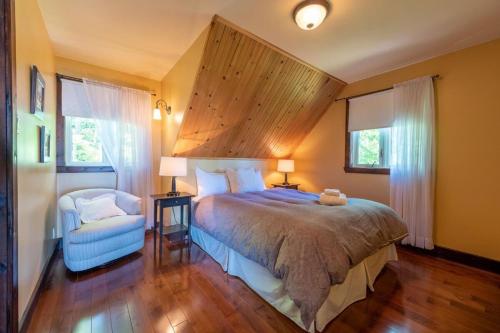 a bedroom with a bed and a chair and two windows at La Grande Ourse de Charlevoix in Petite-Rivière-Saint-François