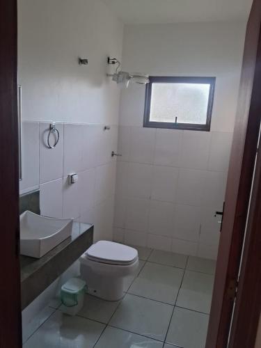 a bathroom with a toilet and a sink and a window at Chácara com Piscina no Centro da Cidade in Socorro
