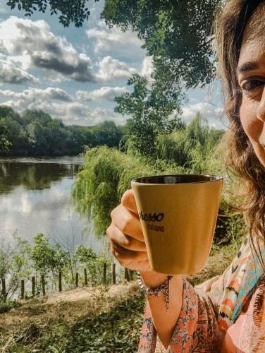 a woman holding a coffee cup in front of a lake at B&B BienViennue in Marcilly-sur-Vienne