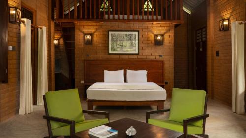 a bedroom with a bed and two green chairs at Ududola Rainforest Cottages in Migahatenna