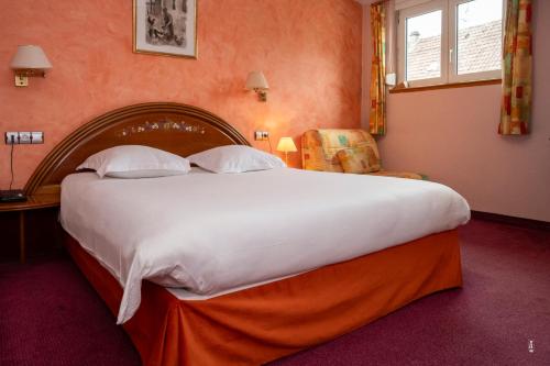 a large white bed in a room with a chair at Logis Hotel Restaurant Le Faudé in Lapoutroie