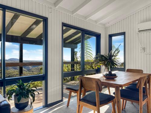 a dining room with a table and chairs and windows at Clifftop cottage escape with breathtaking views in Wentworth Falls