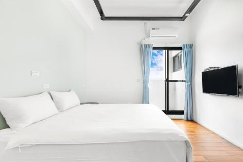 a white bedroom with a bed and a tv at 25Inn Hengchun Kenting in Nanwan