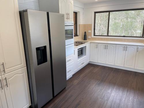 a kitchen with white cabinets and a black refrigerator at Waterfront Paradise with Jetty, BBQ, Pool table, & more in Dora Creek