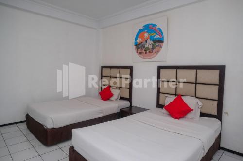two beds in a room with white walls and red pillows at Hotel Candra Kirana Syariah Prawirotaman Yogyakarta Mitra RedDoorz in Yogyakarta