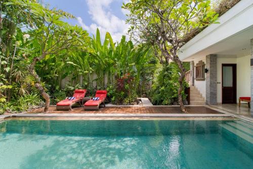 a swimming pool with red chairs next to a house at The Residence Seminyak in Seminyak