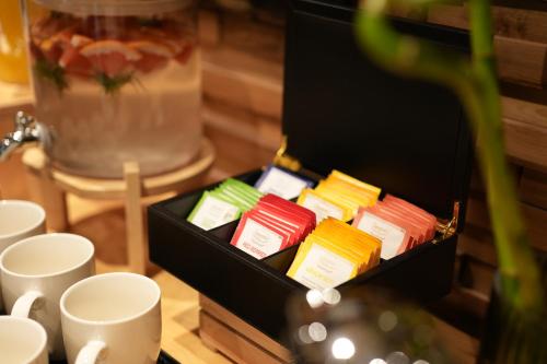 a box filled with different colored packets next to cups at La Suite Boutique Hotel in Tirana