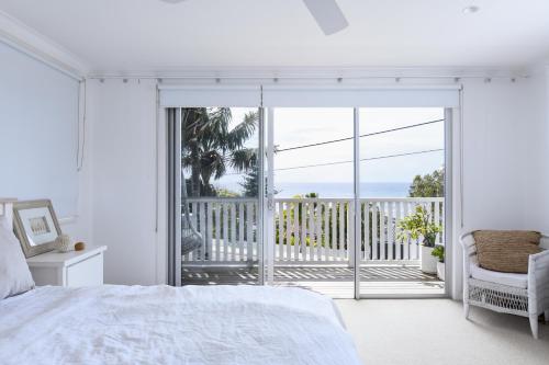a bedroom with a white bed and a balcony at Warriewood beach house in Mona Vale
