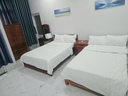 two beds in a room with white sheets at Nhà Khách Hoàng Thắng in Bồng Sơn