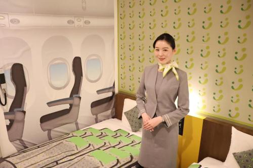 uma mulher de fato ao lado de uma cama em Henn na Hotel Tokyo Haneda em Tóquio