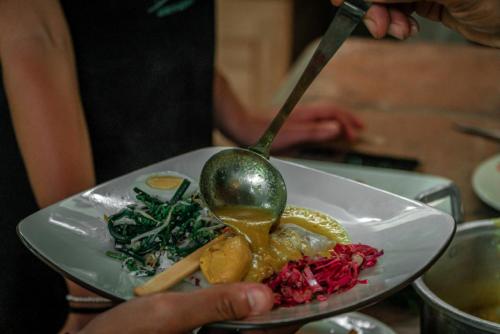 a person holding a plate of food with a spoon at Kebun Kita Ecolodge By Bali Cabin in Padangan