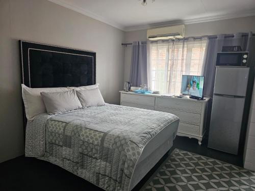 a bedroom with a bed and a dresser and a refrigerator at Arum Lily Guest Rooms in Pretoria