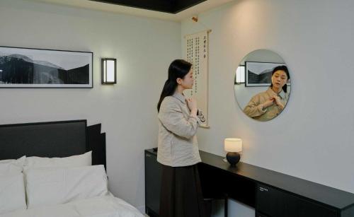 a woman standing in a bedroom looking in a mirror at Aank Hotel and Spa Jongno Unni in Seoul