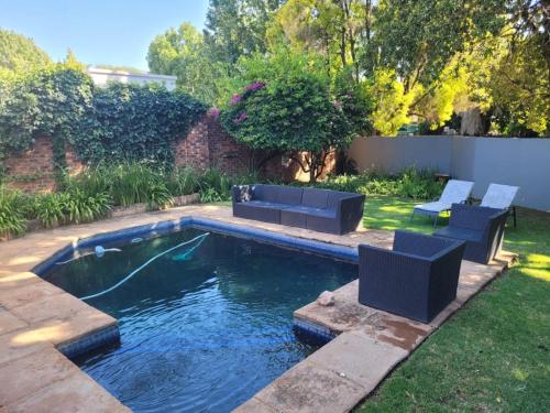 a swimming pool in a yard with two blue chairs at Arum Lily Guest Rooms in Pretoria