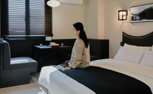 a woman sitting on the edge of a bed at Aank Hotel and Spa Jongno Unni in Seoul