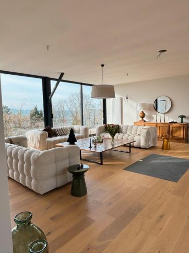 Il comprend un grand salon doté d'un mobilier blanc et de grandes fenêtres. dans l'établissement La Corniche, Villa d'architecte avec piscine, 2mn mer à Houlgate, à Houlgate