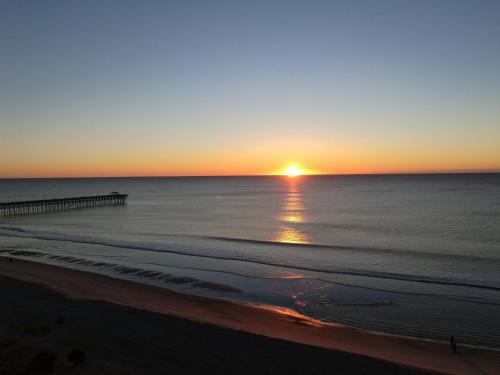 a sunset over the ocean with a pier at Experience the ultimate beachfront lifestyle at Oceans One 1 Bdr, 16th or17th Fl in Myrtle Beach
