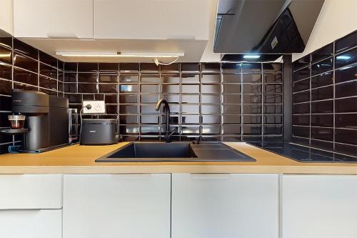 une cuisine avec un évier et un mur carrelé noir dans l'établissement Cozy home Near Paris Fully equipped & decorated, à Bondy