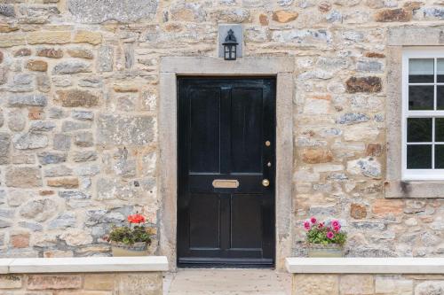 a black door on a stone building with two plants at Two Trees, By Birch Stays in Hetton