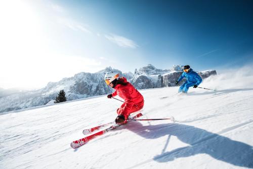 two people are skiing down a snow covered slope at Dolomites Wellness Hotel Savoy in La Villa