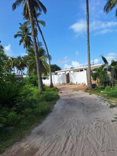 a dirt road in front of a building with palm trees at Private room in Villa Nali in Jambiani