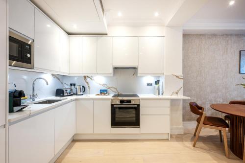a white kitchen with white cabinets and a table at Fountain House Apartments - Hyde Park, London in London