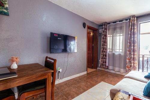 a living room with a table and a tv on the wall at Simba The lion Apartment Mawanda Road in Kampala