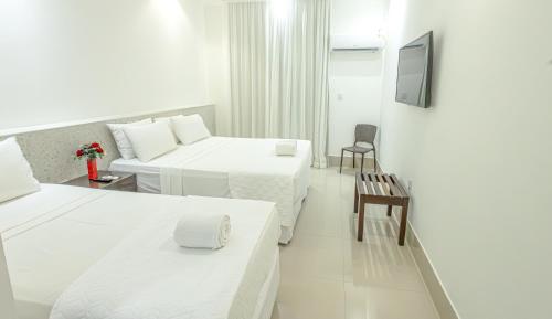 a white hotel room with two beds and a tv at Ramada by Wyndham Porto Seguro Praia in Porto Seguro