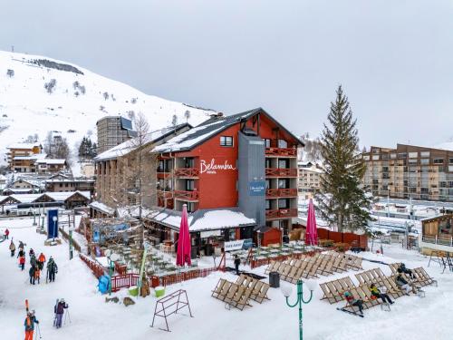 a large red building in the snow with a group of people at Hôtel Les 2 Alpes L'Orée Des Pistes in Les Deux Alpes