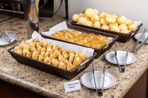 three trays of food sitting on a counter with plates at Park Tower Campinas Residence by Nacional Inn in Campinas