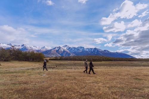 three people walking in a field with mountains in the background at Estancia Patagonia El Calafate - Pristine Luxury Camps in El Calafate