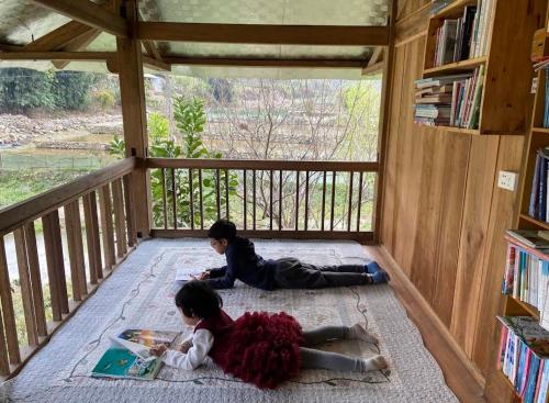 two girls laying on the floor in a room with books at Little House in KhauPha, Mu Cang Chai - homestay, cuisine, cafe in Mù Cang Chải