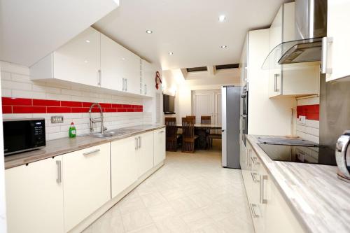 a large kitchen with white cabinets and red accents at Cozy Place in Salford, Sleeps 8, 4 Bedroom, 5 Beds in Manchester
