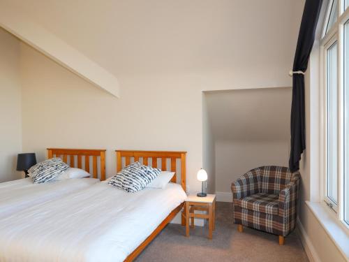 a bedroom with a bed and a chair and a window at Plas Gwylan in Rhosneigr