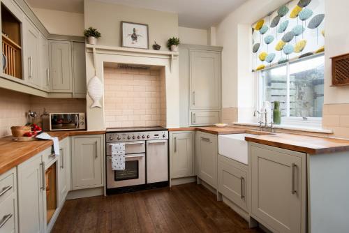 a kitchen with white cabinets and a stove at Pebble Cottage by Coast & Country Stays in Seahouses