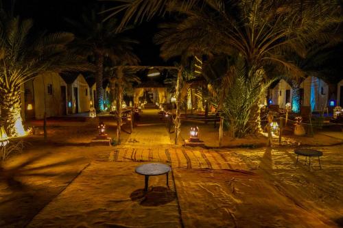 a courtyard with palm trees at night with lights at Sahara Garden Luxury Camp in Merzouga