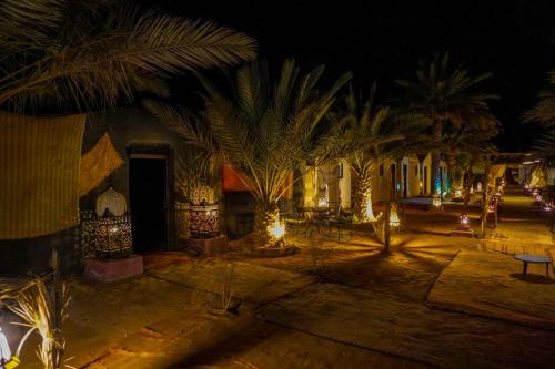 a resort yard at night with palm trees and lights at Sahara Garden Luxury Camp in Merzouga