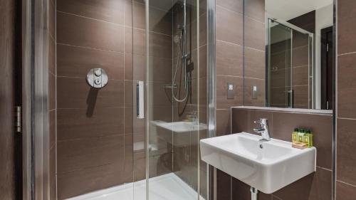 a bathroom with a shower with a sink and a mirror at Cannon Street Serviced Apartments by LovelyStay in London