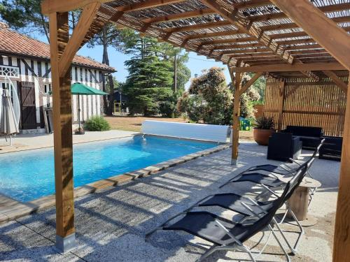 a pool with a wooden pergola and chairs next to it at Cante alaoude in Linxe