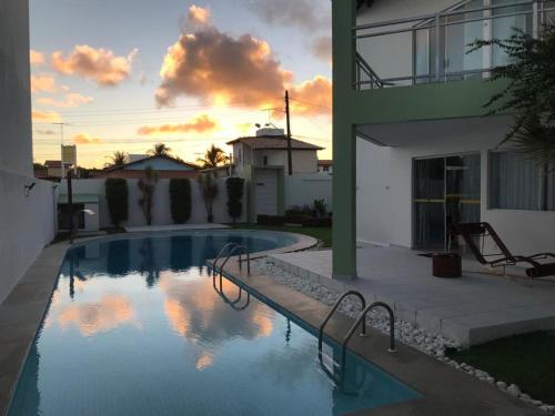 a swimming pool in front of a building with a sunset at Sonho de Verão in Paripueira