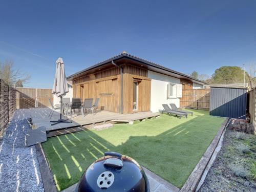 une arrière-cour avec une maison avec une pelouse et un parasol dans l'établissement Le Baleste - Duplex Cosy, à Mimizan